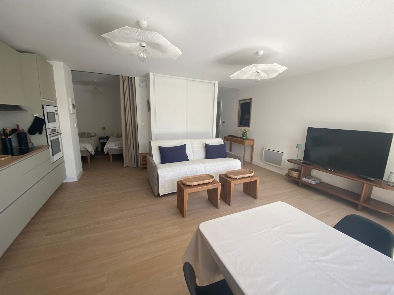 A modern living room with a sofa, a dining table, a TV, and a kitchen area with an oven.