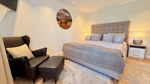 Ein Schlafzimmer mit einem Bett, einem Sessel, einem Nachttisch und einem Wandbild.