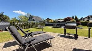 Een achtertuin met een barbecue, lounge stoelen en een verzorgd gazon.
