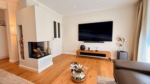 Ein modernes Wohnzimmer mit Kamin, Flachbildfernseher an der Wand und Couchtisch mit Dekoration.