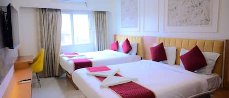 A hotel room with two beds, a desk, a chair, an air conditioning unit, and a television.