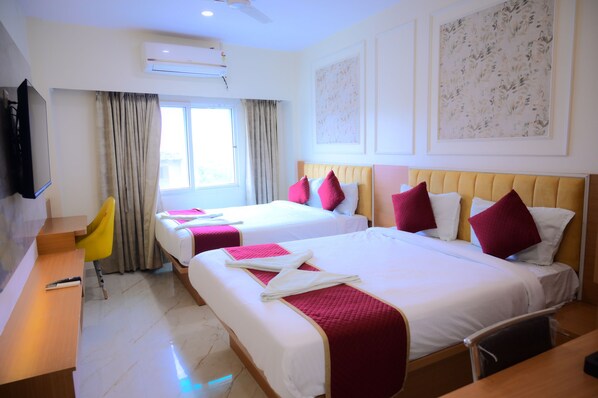 A hotel room with two beds, a desk, a chair, an air conditioning unit, and a television. - Ramanjaneya Executive Hotel (Ayodhya)