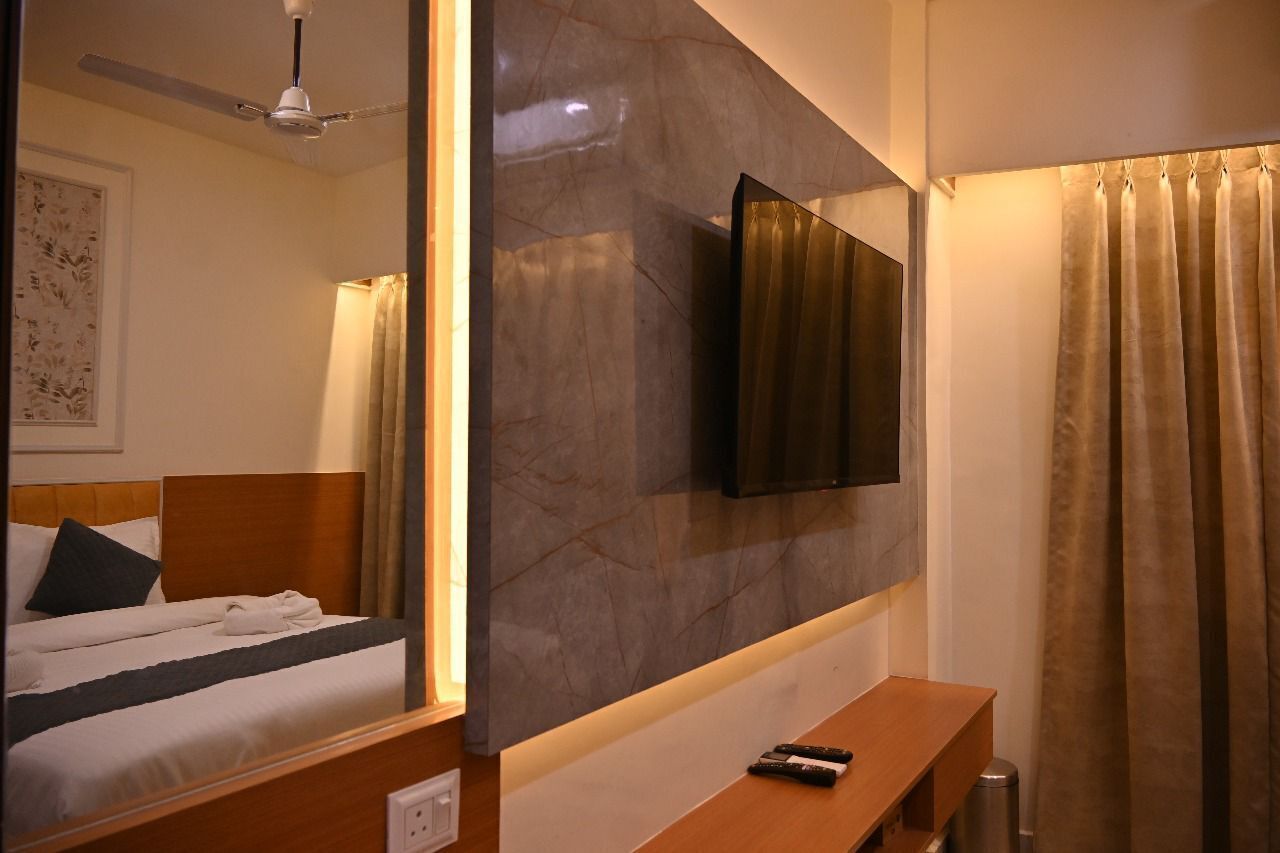 A hotel room with a bed, a bedside table, a TV mounted on the wall, and a shower curtain.