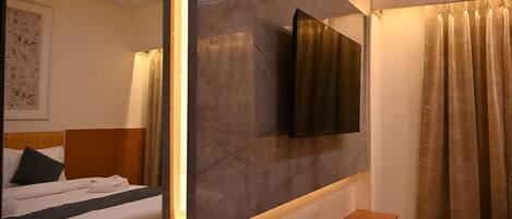 A hotel room with a bed, a bedside table, a TV mounted on the wall, and a shower curtain.
