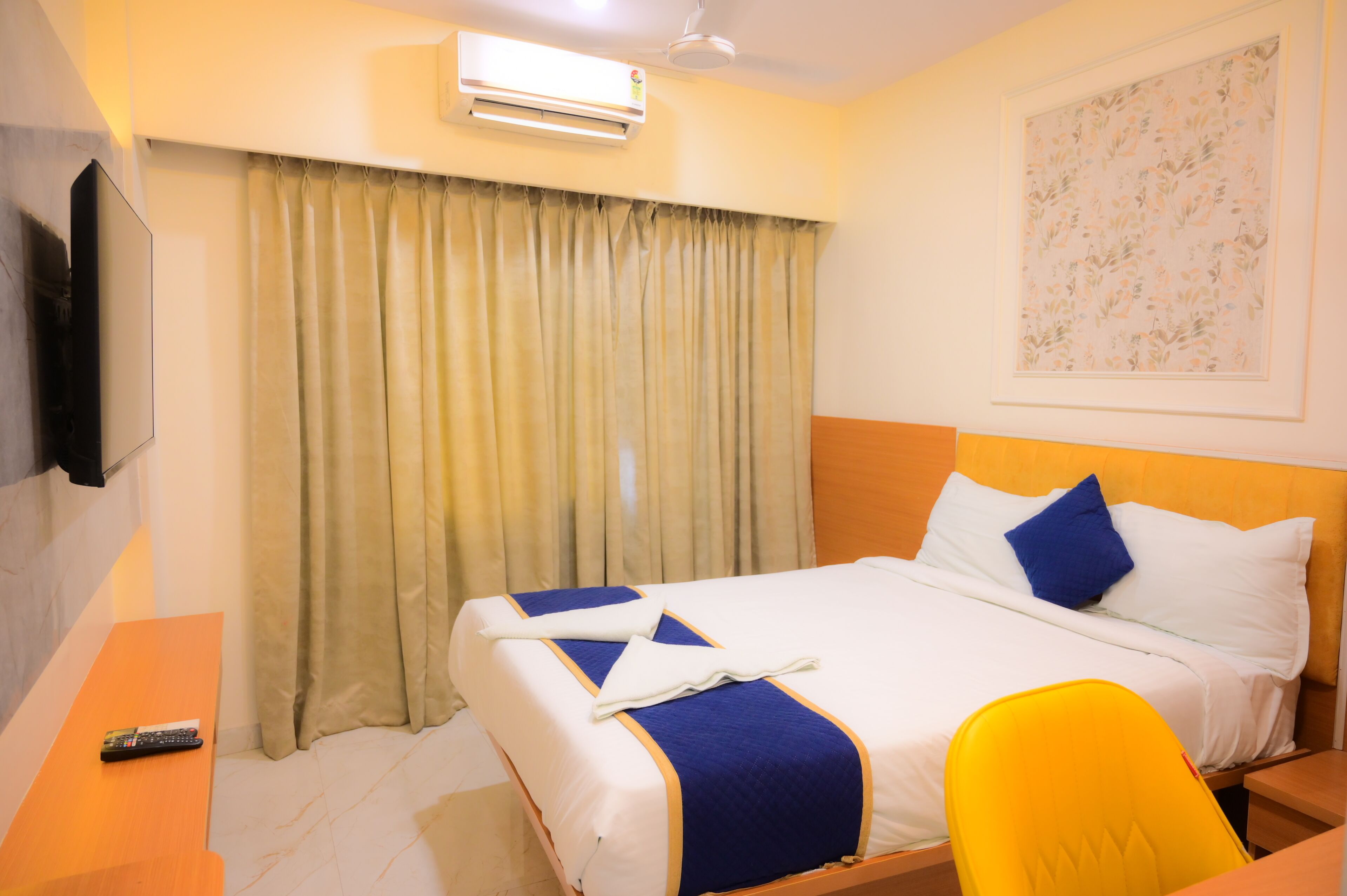 Habitación de hotel con cama, escritorio, silla, televisor y ventana con cortinas.