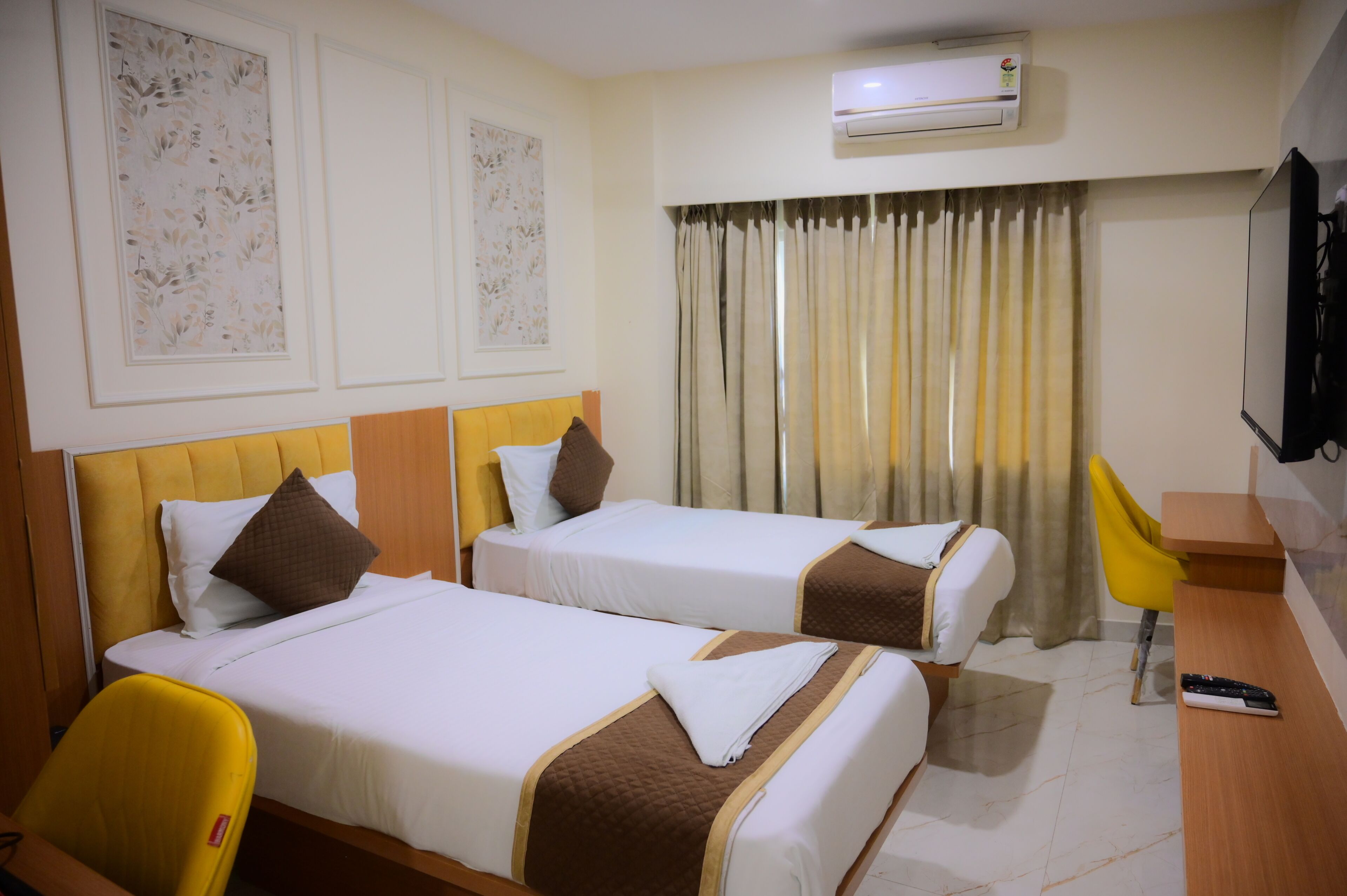 A hotel room with two beds, a desk, a chair, an air conditioning unit, and a television.