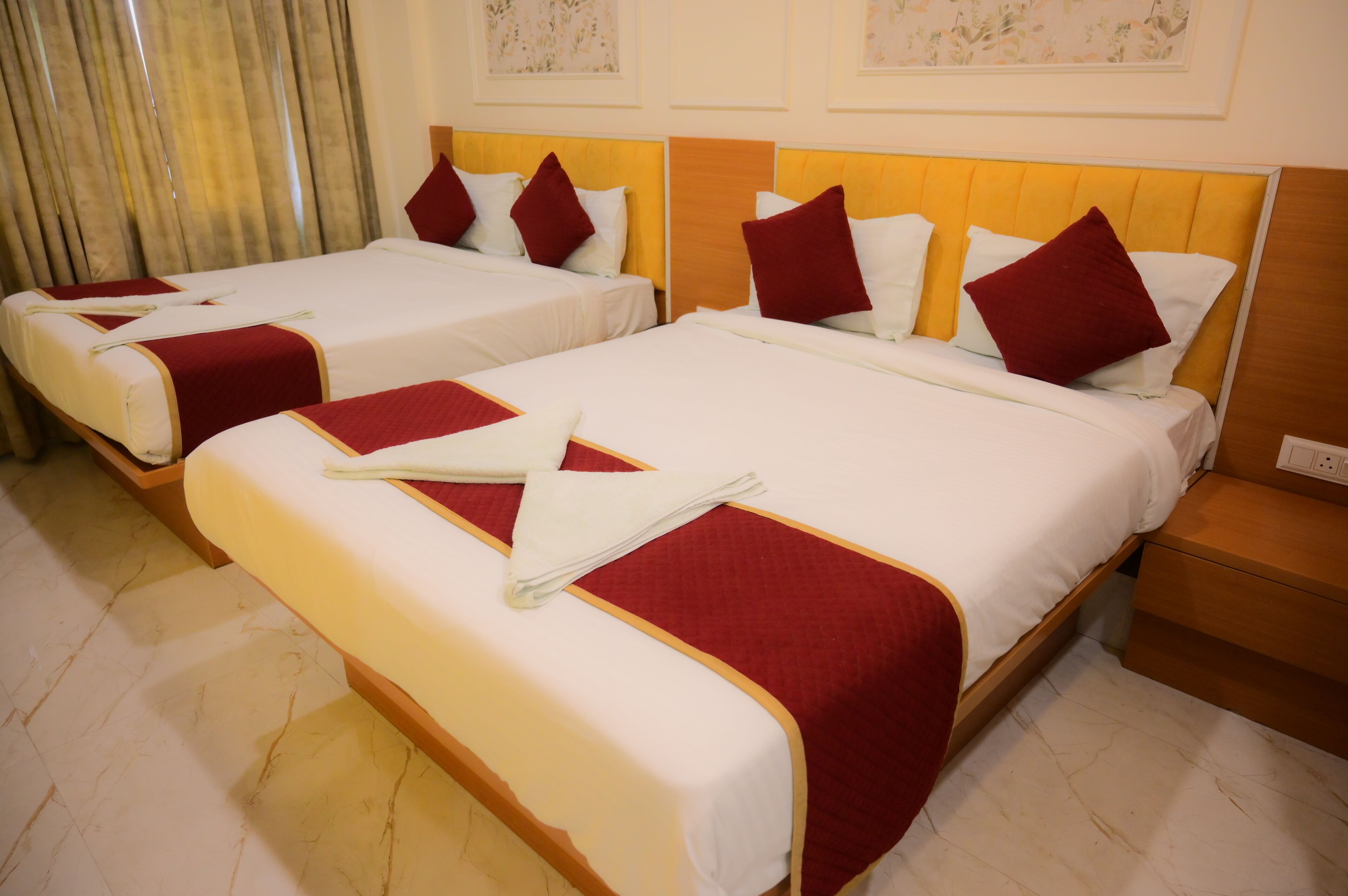 Habitación de hotel con dos camas, cada una con ropa blanca y detalles rojos, cabeceros de madera y piso de mármol.