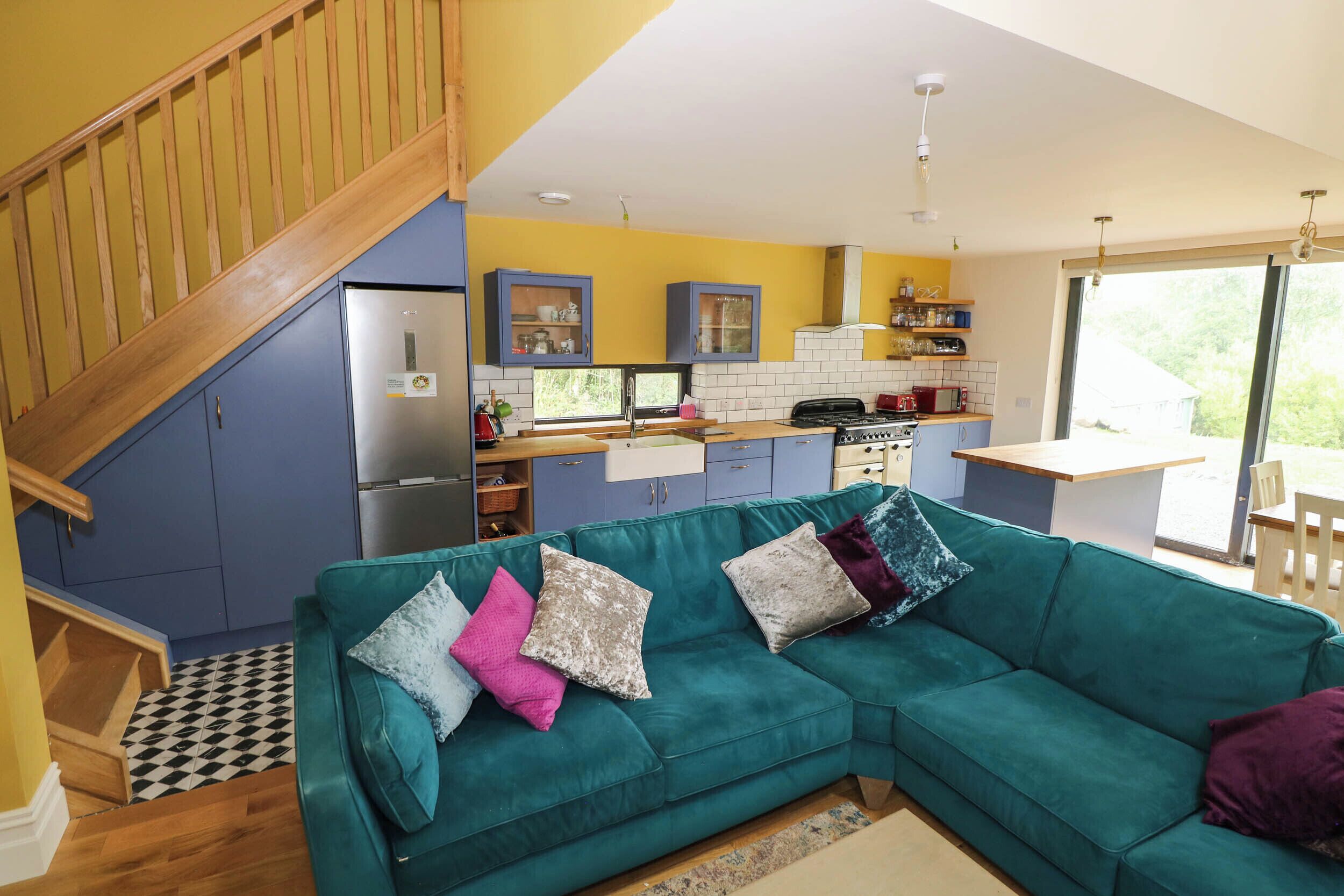 A modern kitchen with a built-in stove, a dining area with a wooden table, and a teal sofa with cushions.
