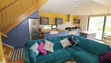 A modern kitchen with a built-in stove, a dining area with a wooden table, and a teal sofa with cushions.