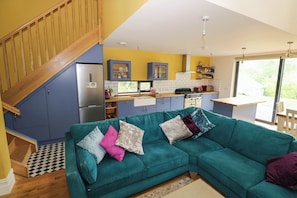 A modern kitchen with a built-in stove, a dining area with a wooden table, and a teal sofa with cushions.