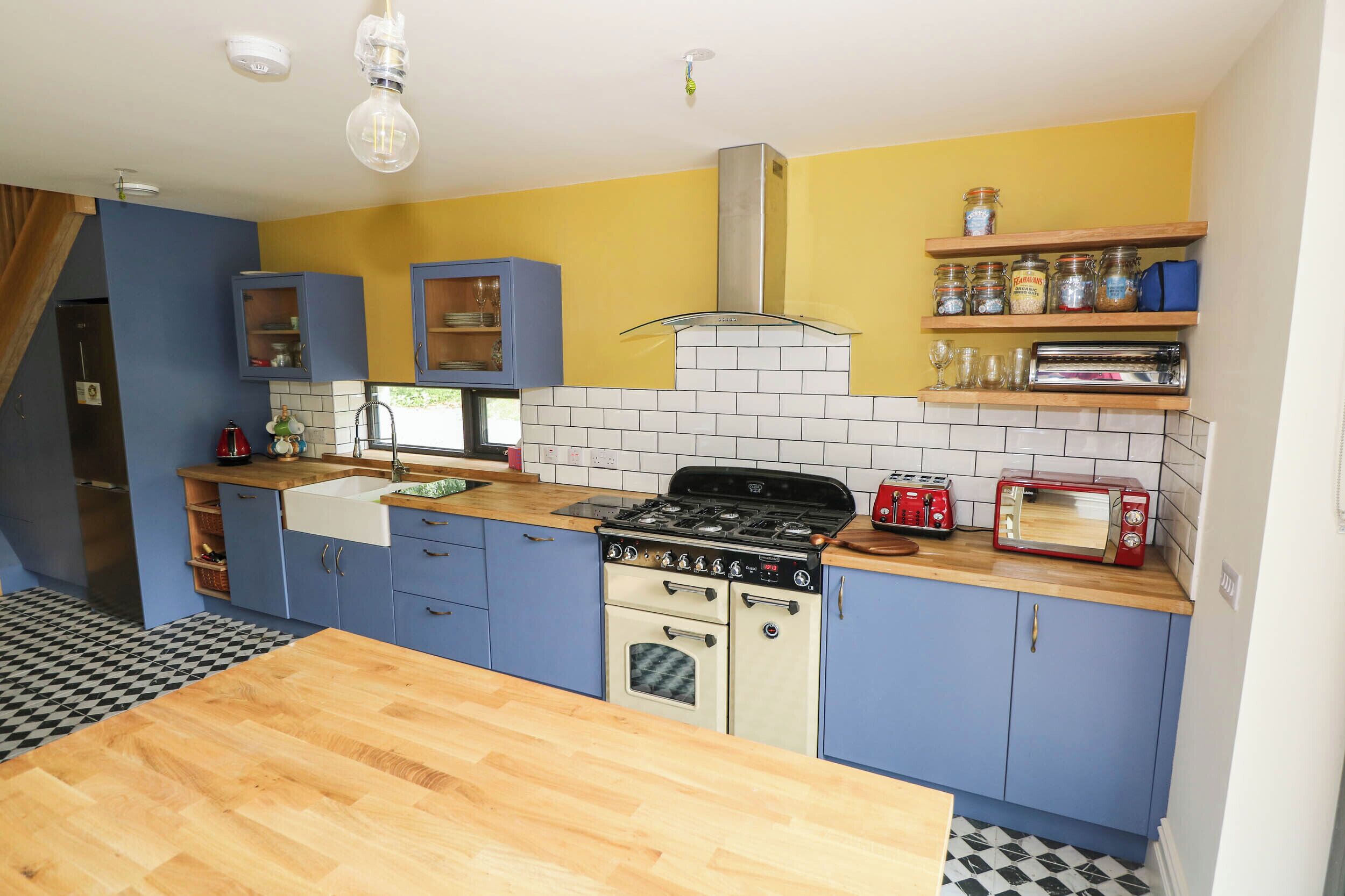 A compact kitchen with blue cabinets, a wooden countertop, a stove, and a red toaster.