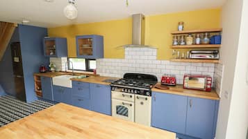 A compact kitchen with blue cabinets, a wooden countertop, a stove, and a red toaster.