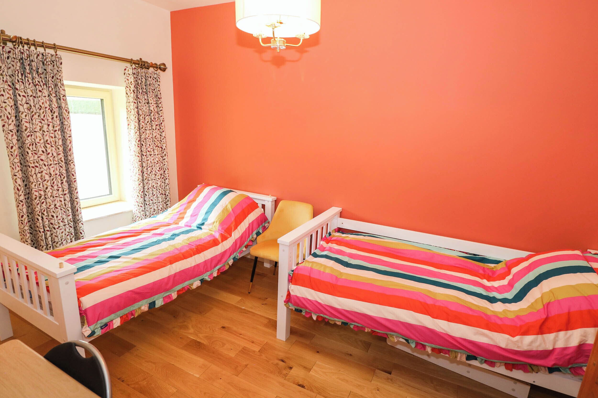 A room with two single beds, a window with curtains, a chair, and a chandelier.
