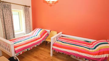 A room with two single beds, a window with curtains, a chair, and a chandelier.