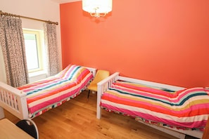 A room with two single beds, a window with curtains, a chair, and a chandelier.