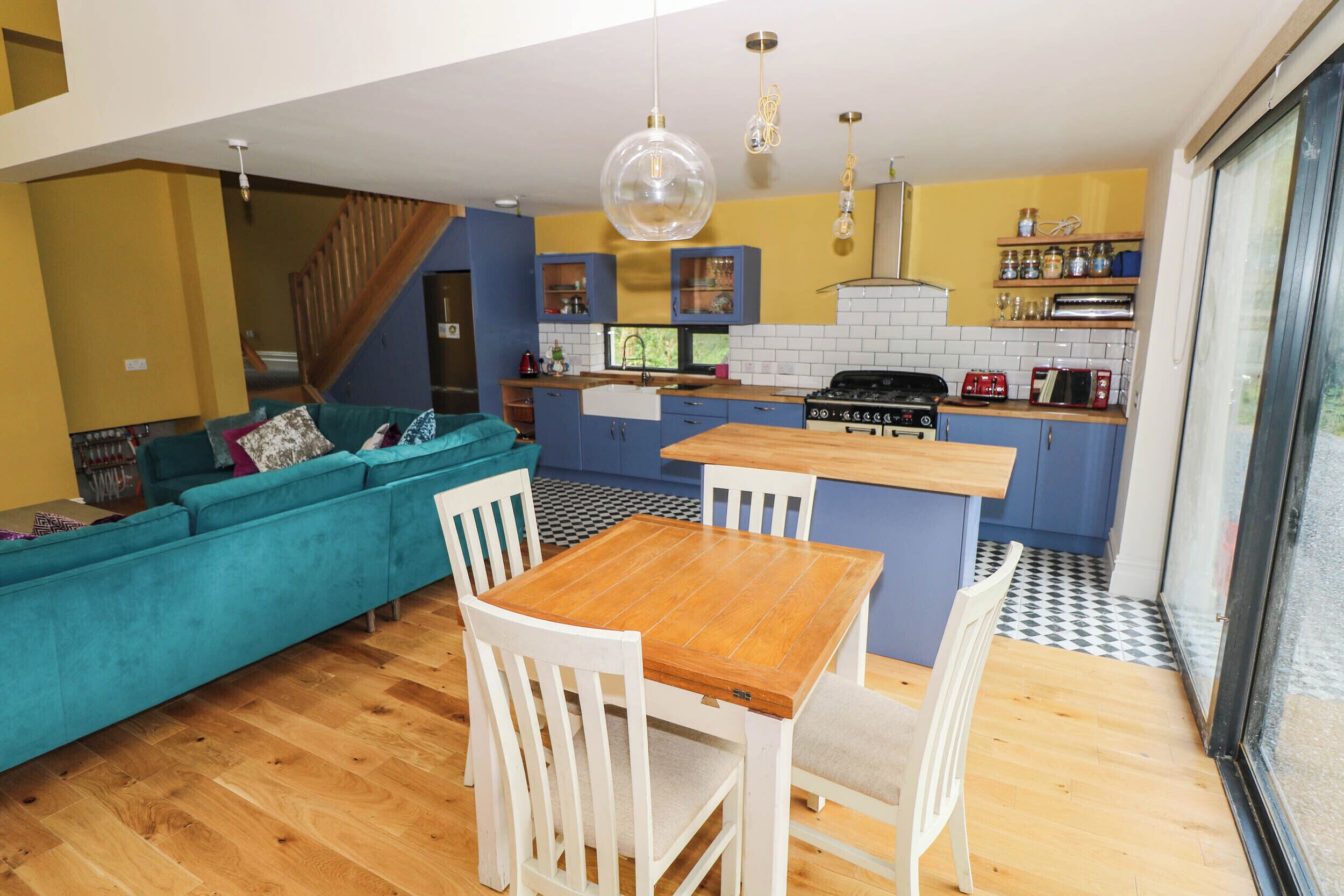 Une cuisine moderne avec un coin repas, un escalier et un salon doté d’un canapé de couleur turquoise.