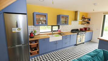 Cocina compacta con refrigerador, estufa, lavaplatos y gabinetes azules.