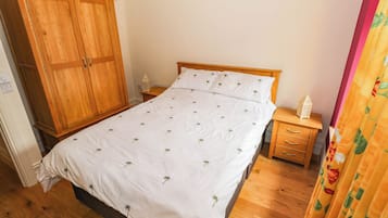 Une chambre à coucher avec une armoire en bois, un lit simple avec une literie blanche, une table de chevet et une petite table sur laquelle est posé un objet décoratif.