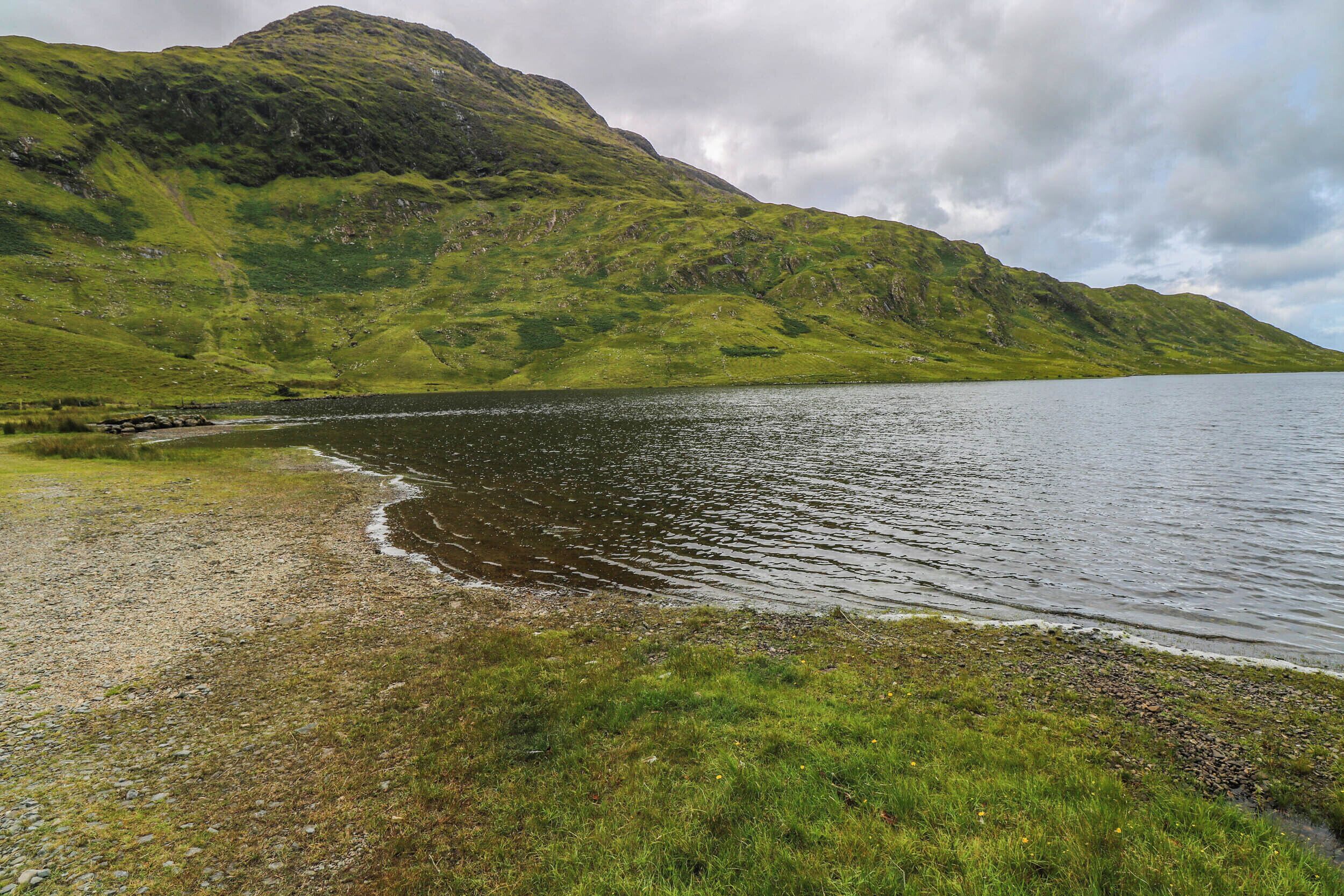 A natural landscape with a lake, grassy shores, and a mountain in the background.
