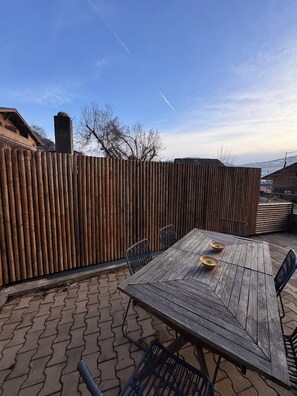 Eine Terrassengaststätte mit Holztisch und -stühlen, einem Bambuszaun und Blick auf eine verschneite Landschaft.