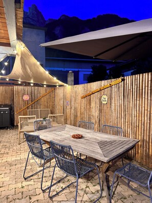 Ein Außenbereich mit Essbereich, einem Holztisch und -stühlen, einem Grill und einem Bambuszaun.