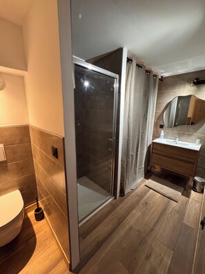 Ein modernes Badezimmer mit einer gläsernen Duschkabine, einem Holzwaschtisch und einem Spiegel über dem Waschbecken.