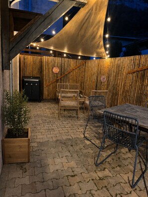 Eine Außenpatio mit Holztisch und -stühlen, einem Grill und einer Bambuswand.