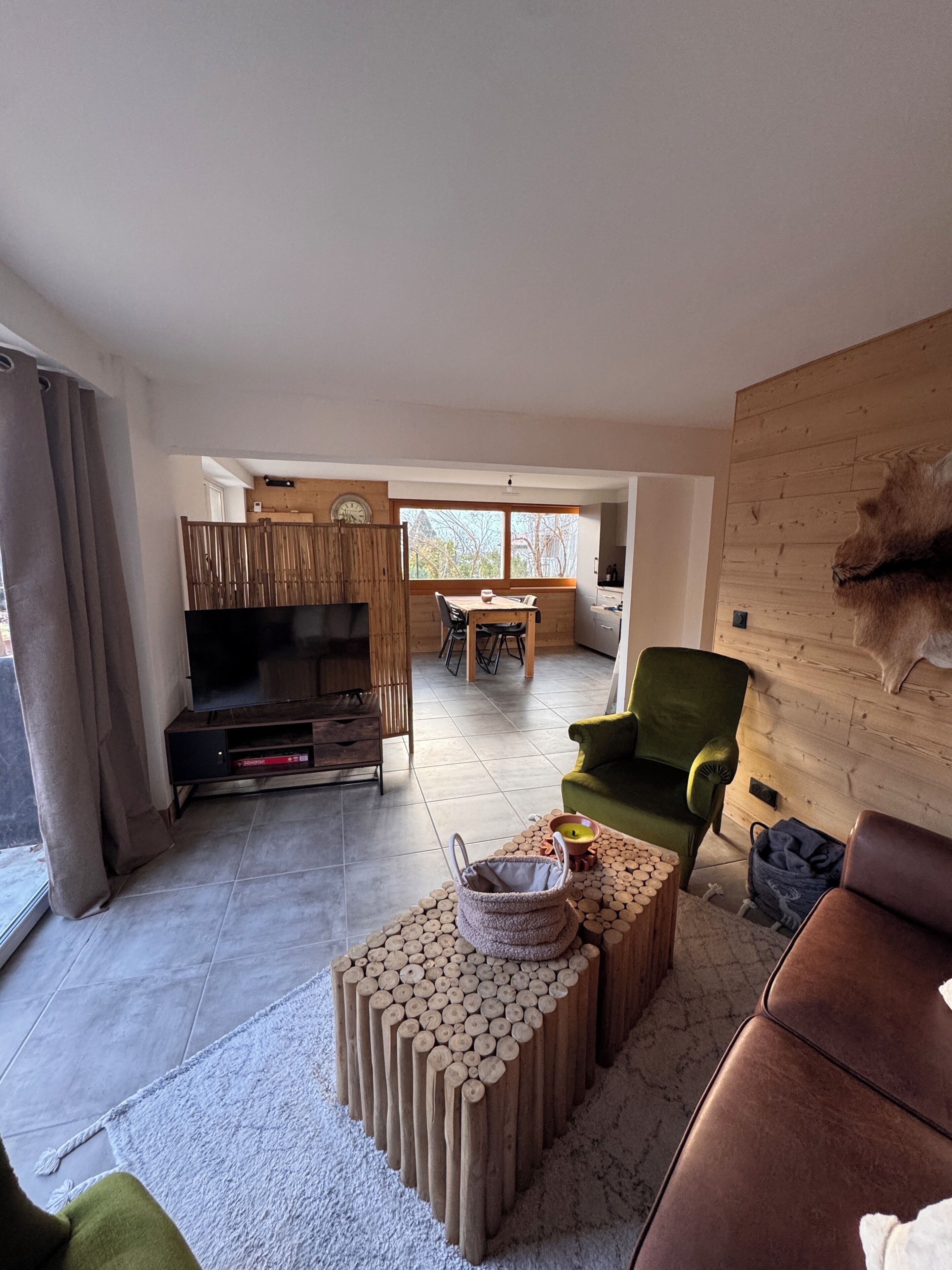 A modern living room with a flat-screen TV, a wooden coffee table, and a green armchair.