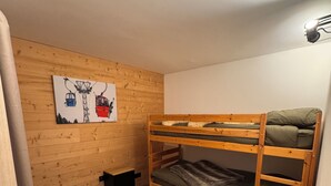 Quarto com beliche, paredes de madeira, um banquinho preto e uma pintura de um teleférico de esqui.