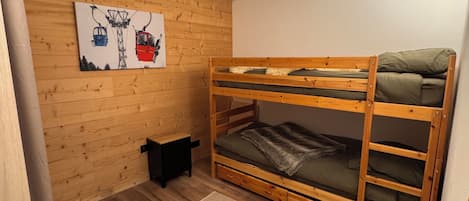 A bunk bed room with wooden walls, a small black stool, and a painting of a ski lift.