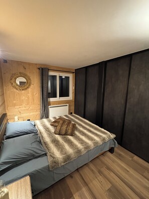 Ein Schlafzimmer mit einem Bett, einem Fenster, einer Heizung und einer Holzwand.