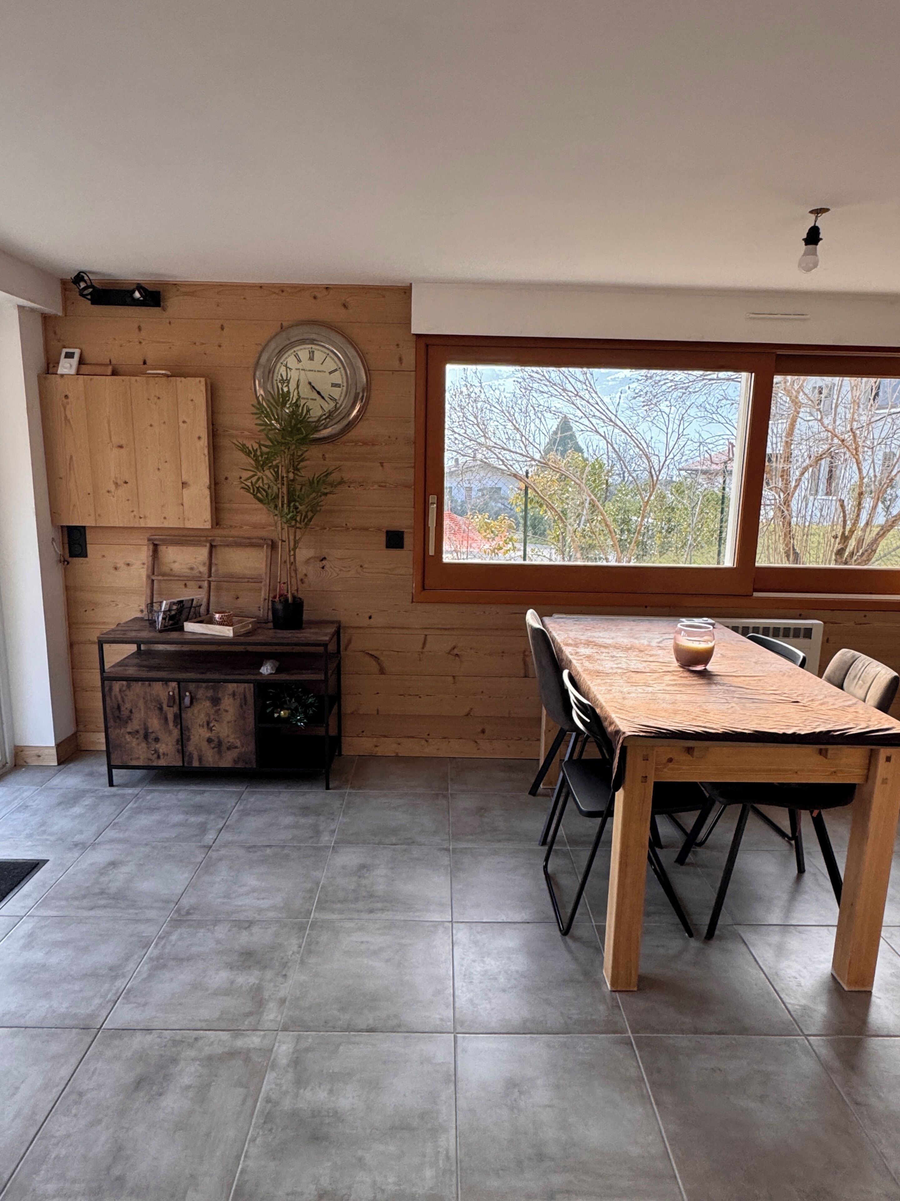 A modern kitchen with a wooden cabinet, a clock, and a dining area with a table and chairs.
