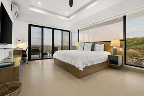 A modern hotel room with a large bed, a desk, a chair, and a TV. There is a balcony with a view of the landscape. - Villa Oceana | 5 Suites , Ocean Views, Club Access (Playas del Coco)