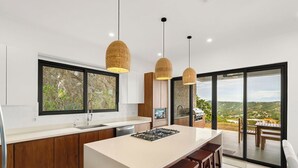 Een moderne keuken met een centraal eiland, houten keukenkastjes en grote ramen met uitzicht op het landschap.