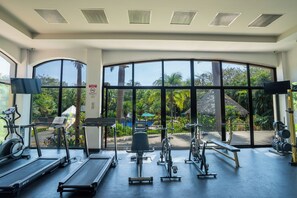 A gym with treadmills, stationary bikes, and weight machines, large windows with a view of a pool and greenery.