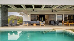 Ein moderner Poolbereich im Freien mit einer Couch, Stühlen und einem Holztisch.