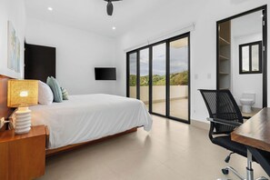 A bedroom with a bed, a desk, a chair, a television, and a sliding glass door leading to an outdoor area.