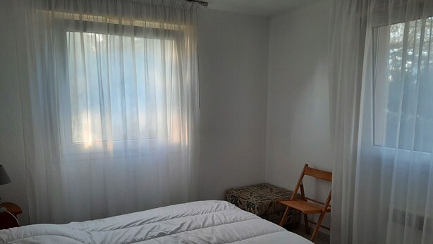 A bedroom with a bed, a chair, and a window with sheer curtains. - Residence with a pool next to the Moliets Golf Course; Duplex apartment for 8–9 people, 10 minutes from the ocean (Moliets-et-Maa)