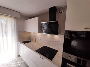 A modern kitchen with white cabinets, a black countertop, and a built-in oven. - Residence with a pool next to the Moliets Golf Course; Duplex apartment for 8–9 people, 10 minutes from the ocean (Moliets-et-Maa)