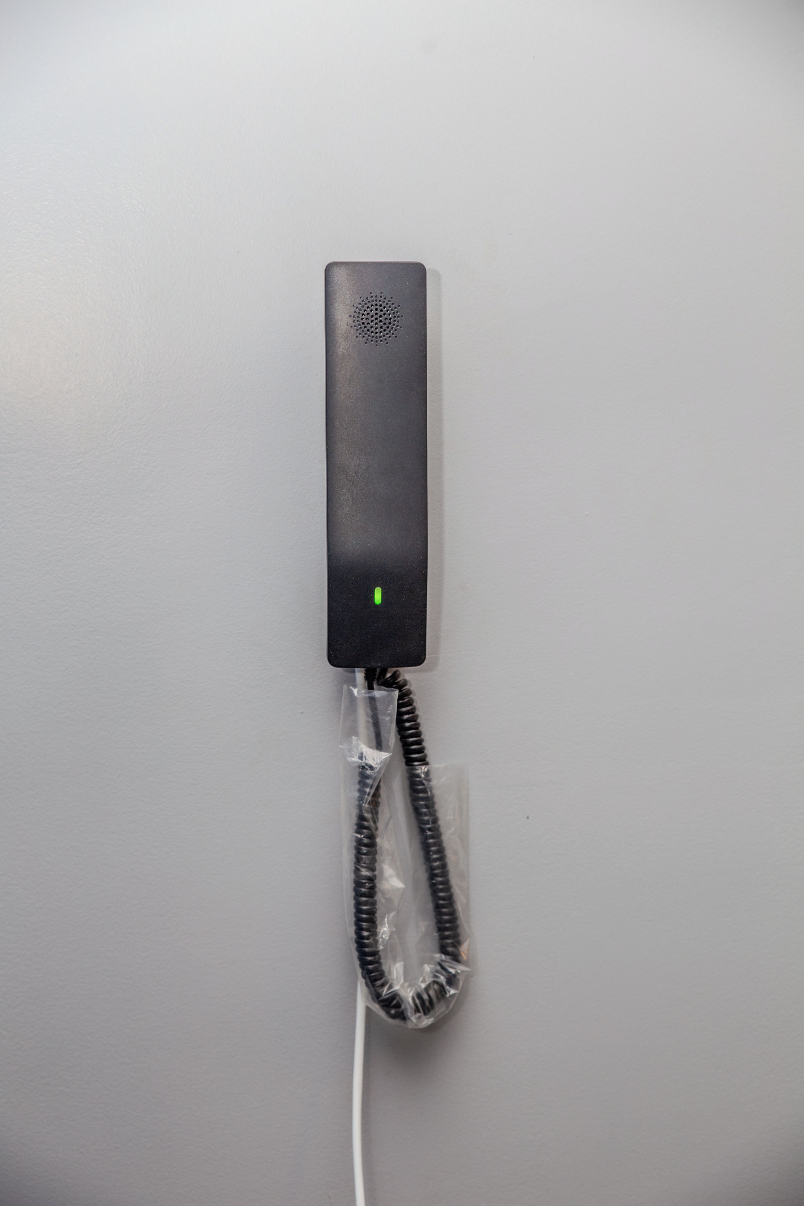 Een zwarte telefoon met een opgerolde kabel en een groene indicatorlamp, geplaatst op een egaal oppervlak.