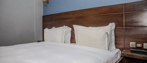 A hotel room with a wooden headboard, white bedding, and a nightstand with a phone and a switch.