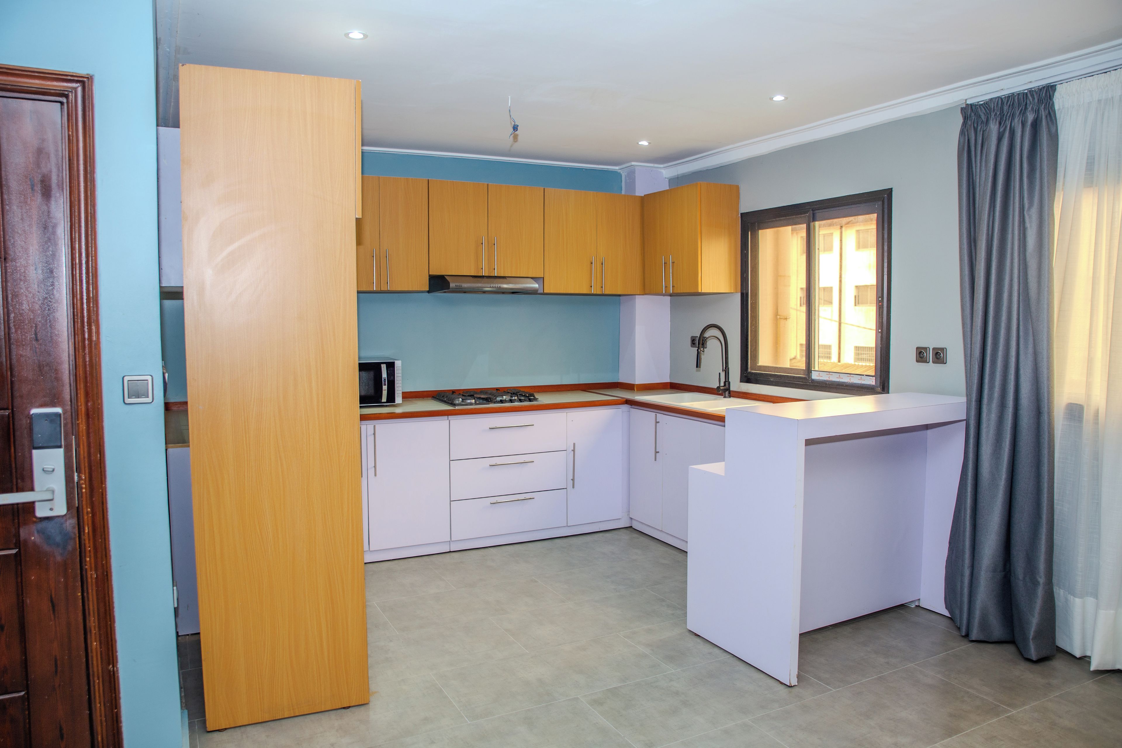 A compact kitchen with wooden cabinets, a built-in microwave, and a window with curtains.