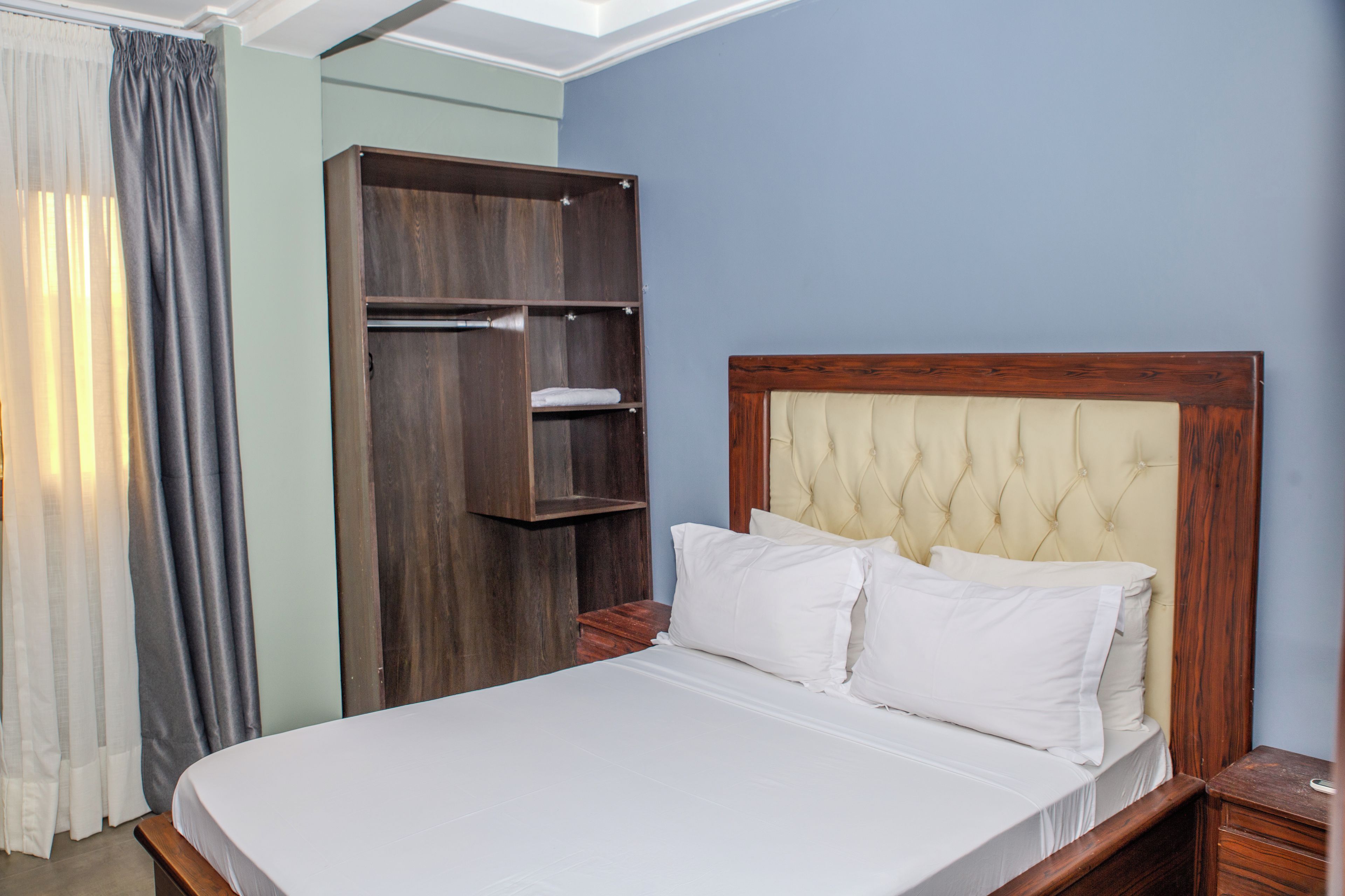 A hotel room with a bed, a wooden wardrobe, and a nightstand.