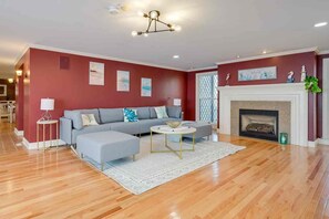 A living room with a sofa, ottoman, coffee table, fireplace, and artwork on the walls. - 1 Mi to Beach: Spacious 5-bedroom house in terrific Sandwich with AC (Sandwich)