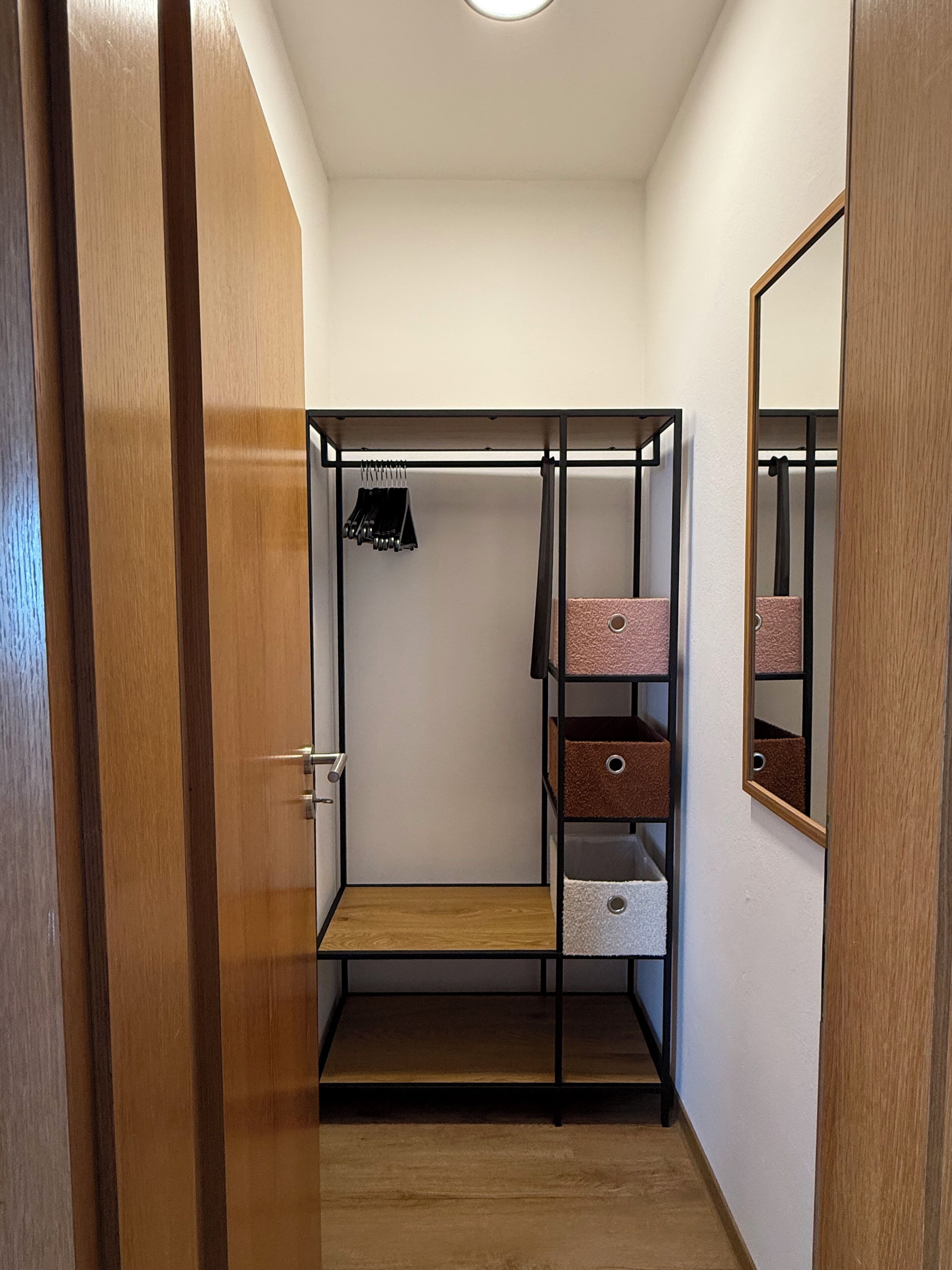 Ein begehbarer Kleiderschrank mit Metallregalen, einem Spiegel und einer Holztür.