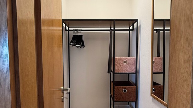 A walk-in closet with metal shelving, a mirror, and a wooden door. - Apartment with a large terrace and a view of the Black Forest (Willstätt)