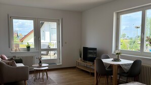 A bedroom with two beds, a TV, a dining table with chairs, and a sofa. - Apartment with a large terrace and a view of the Black Forest (Willstätt)