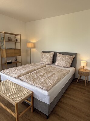 Ein Doppelbett mit floraler Bettwäsche, ein Nachttisch, eine Lampe und ein Holzregal.