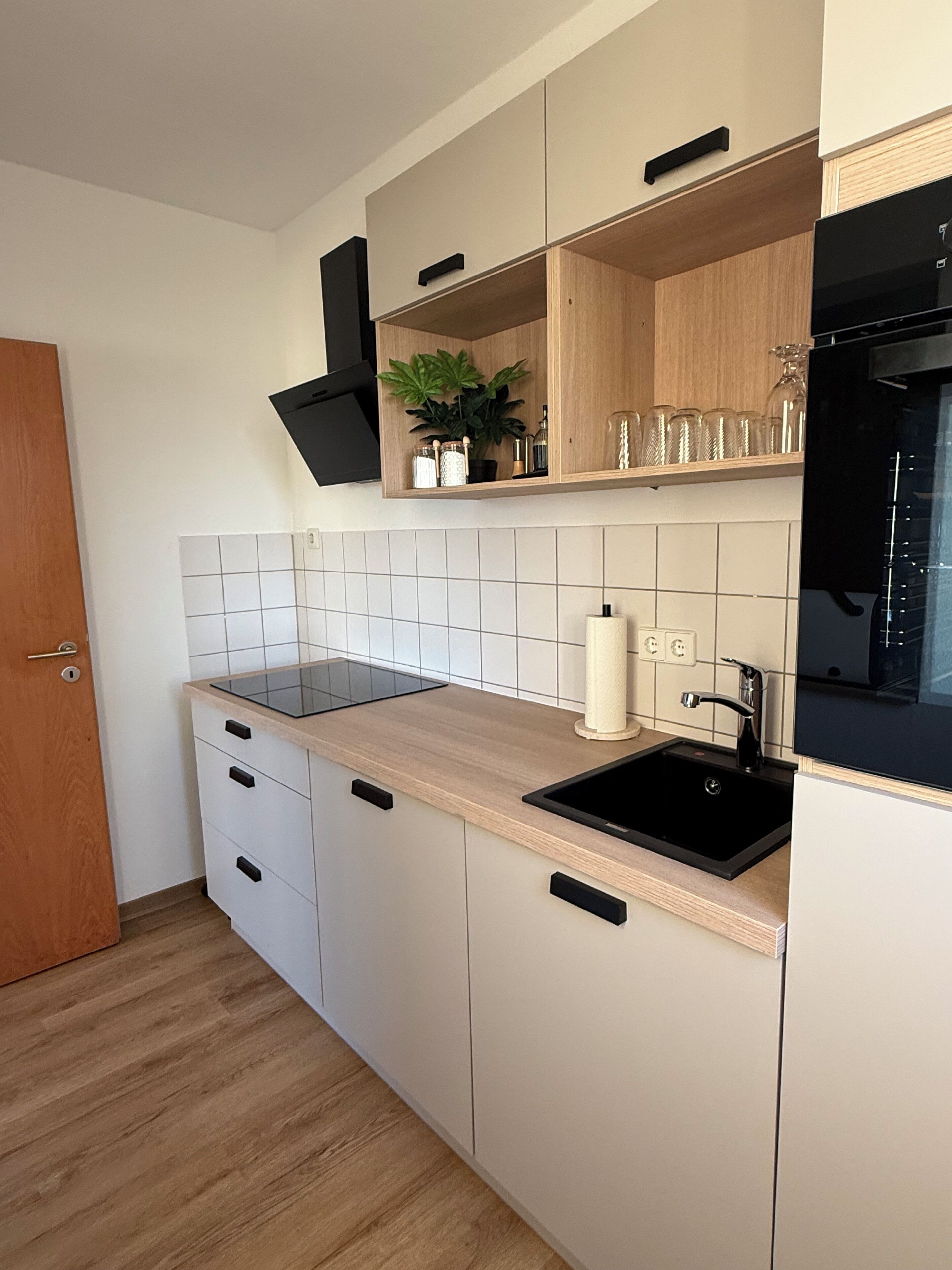 Eine moderne Küche mit einem schwarzen Spülbecken, Holzschränken, einer Arbeitsplatte und einem eingebauten Backofen.