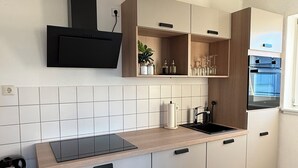 A modern kitchen with a built-in oven, a black range hood, and a countertop with a sink. - Apartment with a large terrace and a view of the Black Forest (Willstätt)